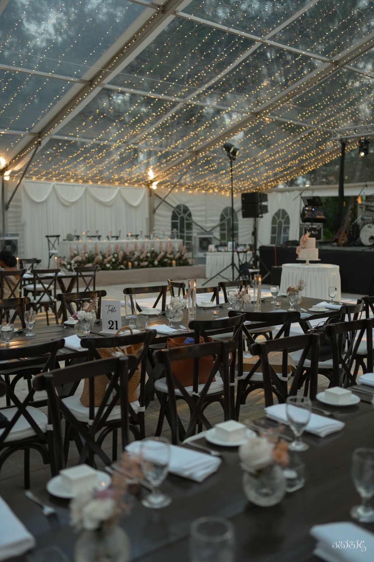 Long tables and gold chairs set for an outdoor wedding reception beneath the transparent marquee at Ten Acres
